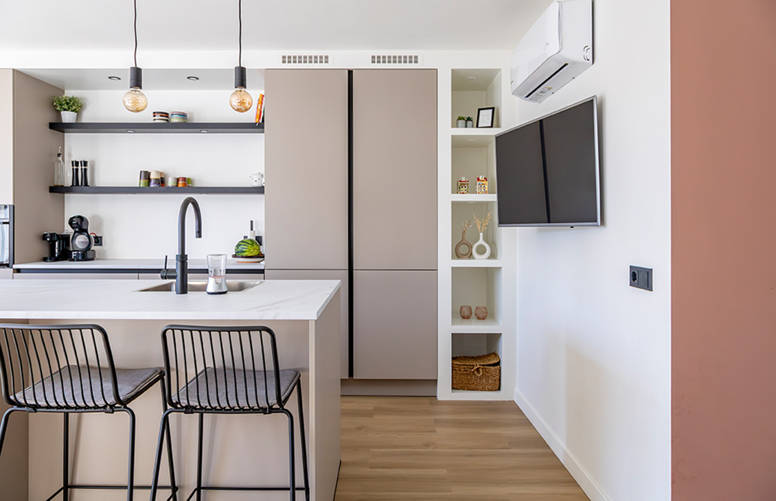 Moderne keuken met beige kasten, wit keukenblad, keukeneiland, zwarte kraan en tv in de keuken