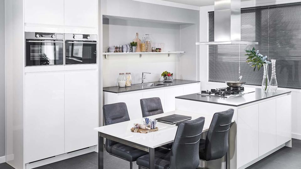 Hoogglans witte keuken met eiland en kastenwand.