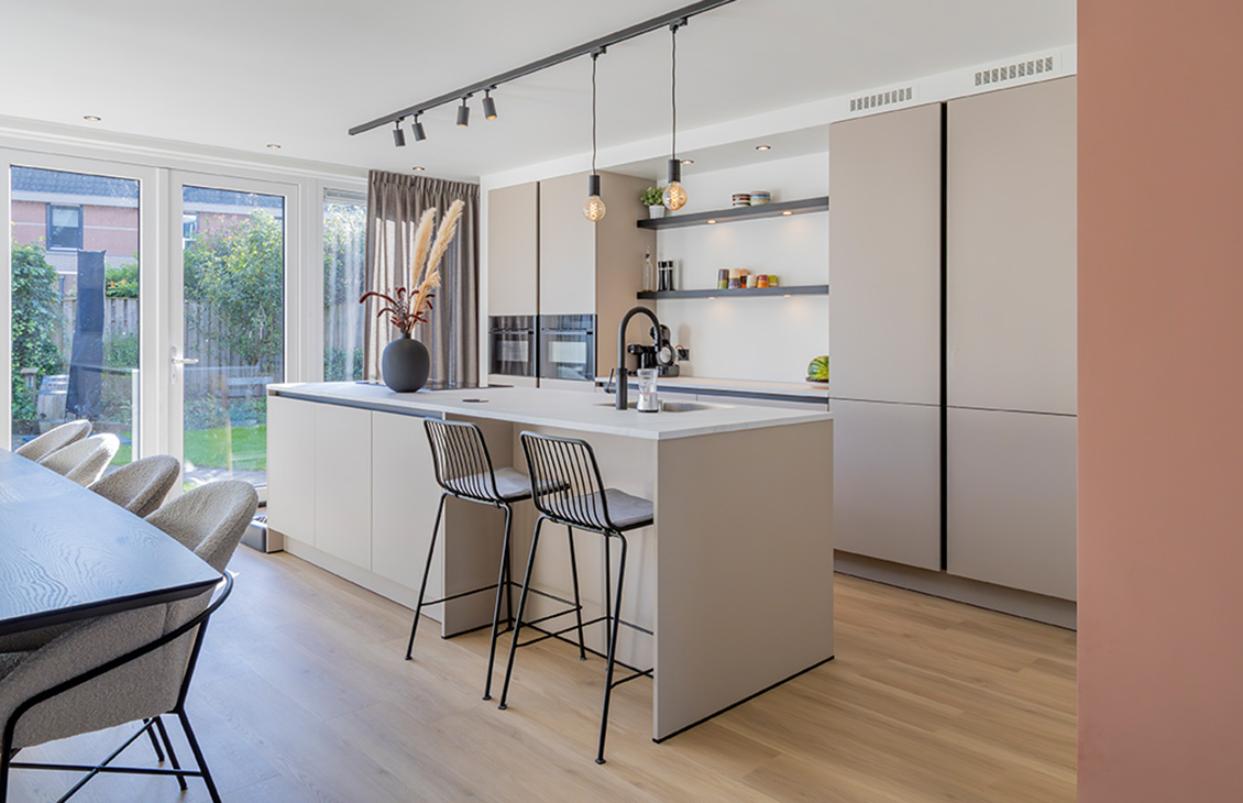 Moderne keuken met beige kasten, wit keukenblad, keukeneiland met zwarte barkrukken, hanglampen