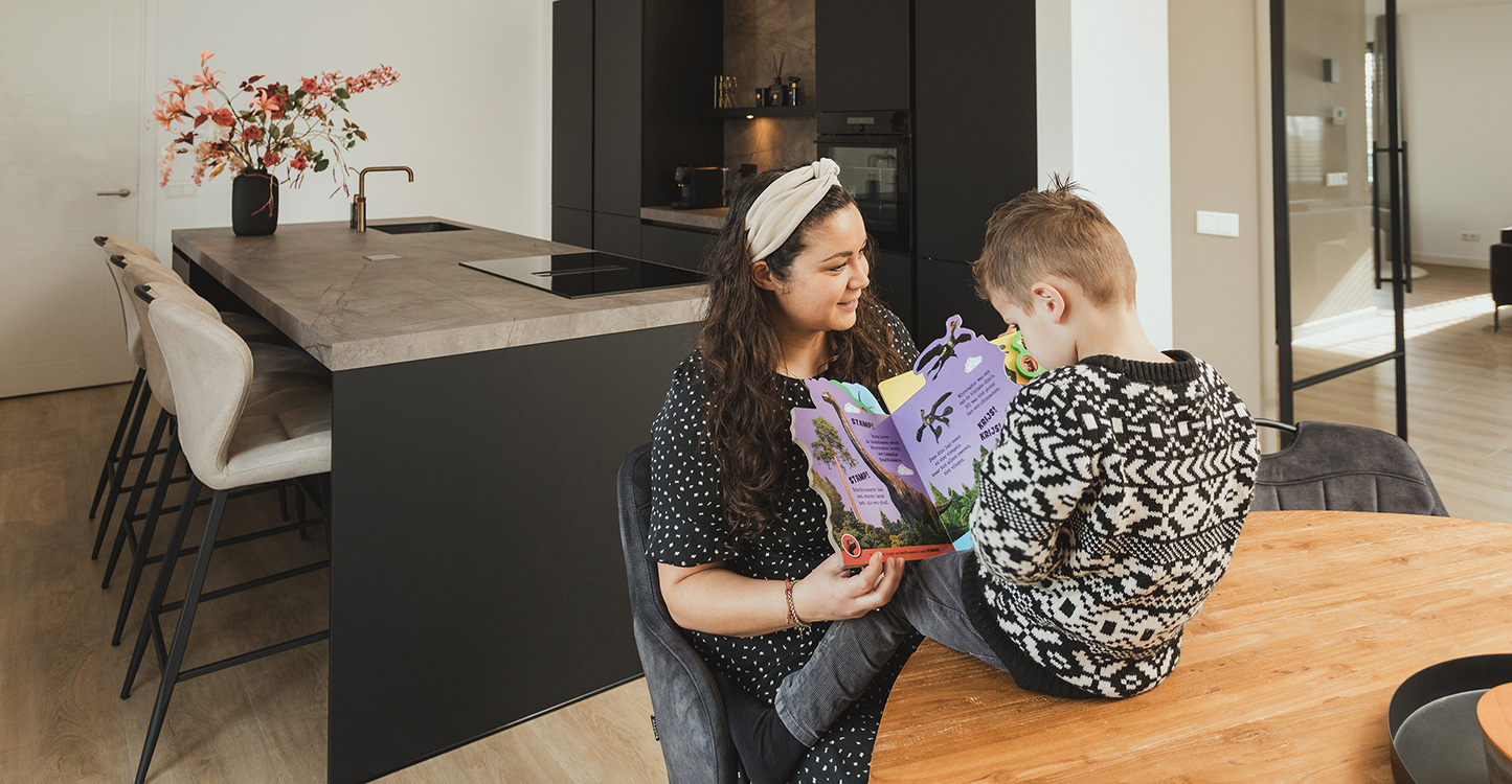 Mevrouw Remijnse met kind. Kind zit op tafel en mevrouw leest boek voor