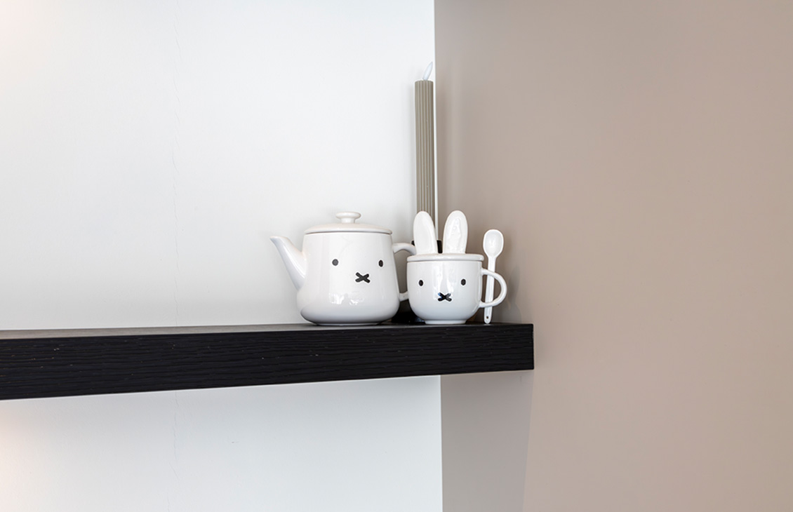 Moderne keuken met beige kasten, wit keukenblad, keukeneiland met zwarte barkrukken, hanglampen, en zicht op een tuin